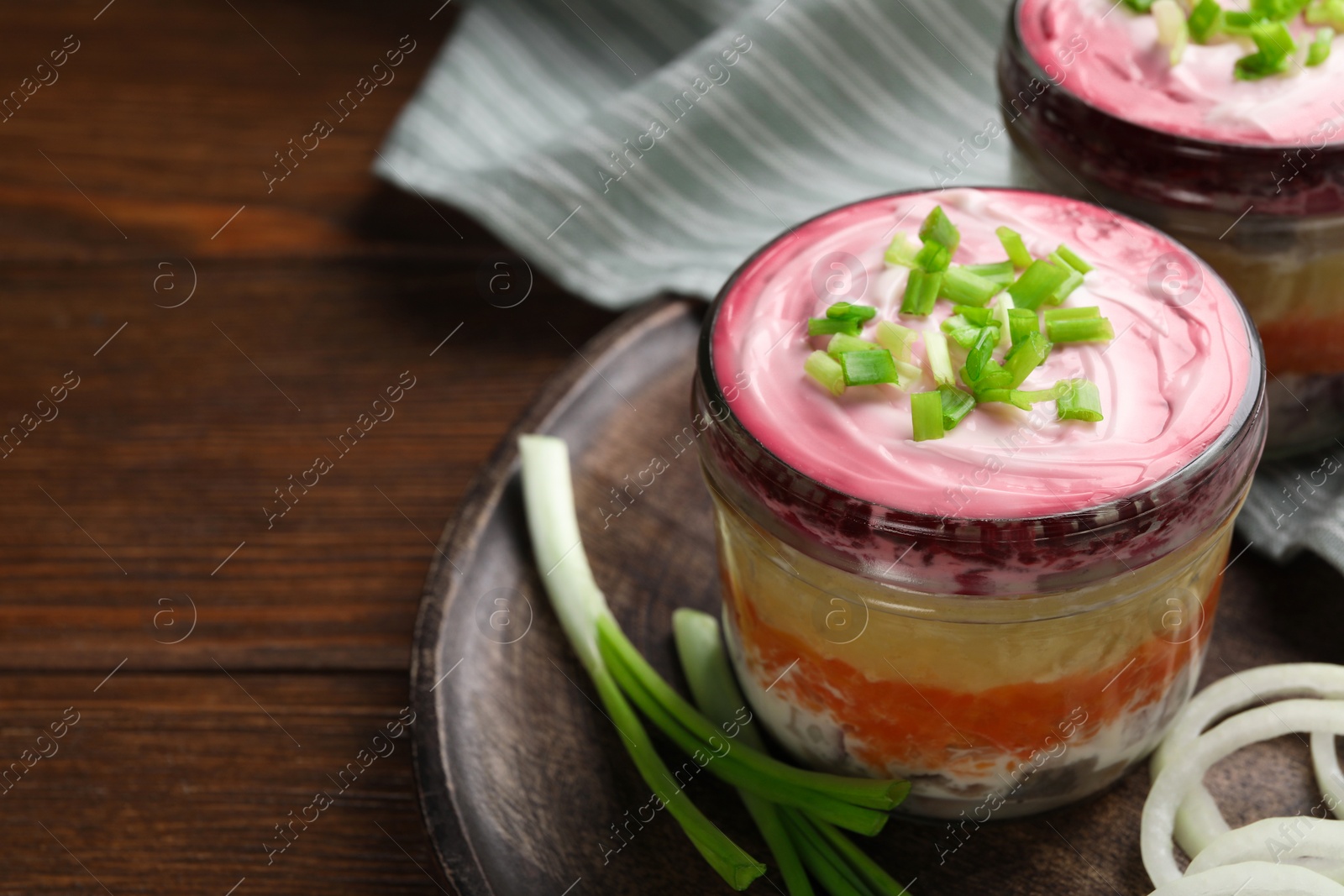 Photo of Tray with glass jars of herring under fur coat on wooden table, space for text. Traditional Russian salad