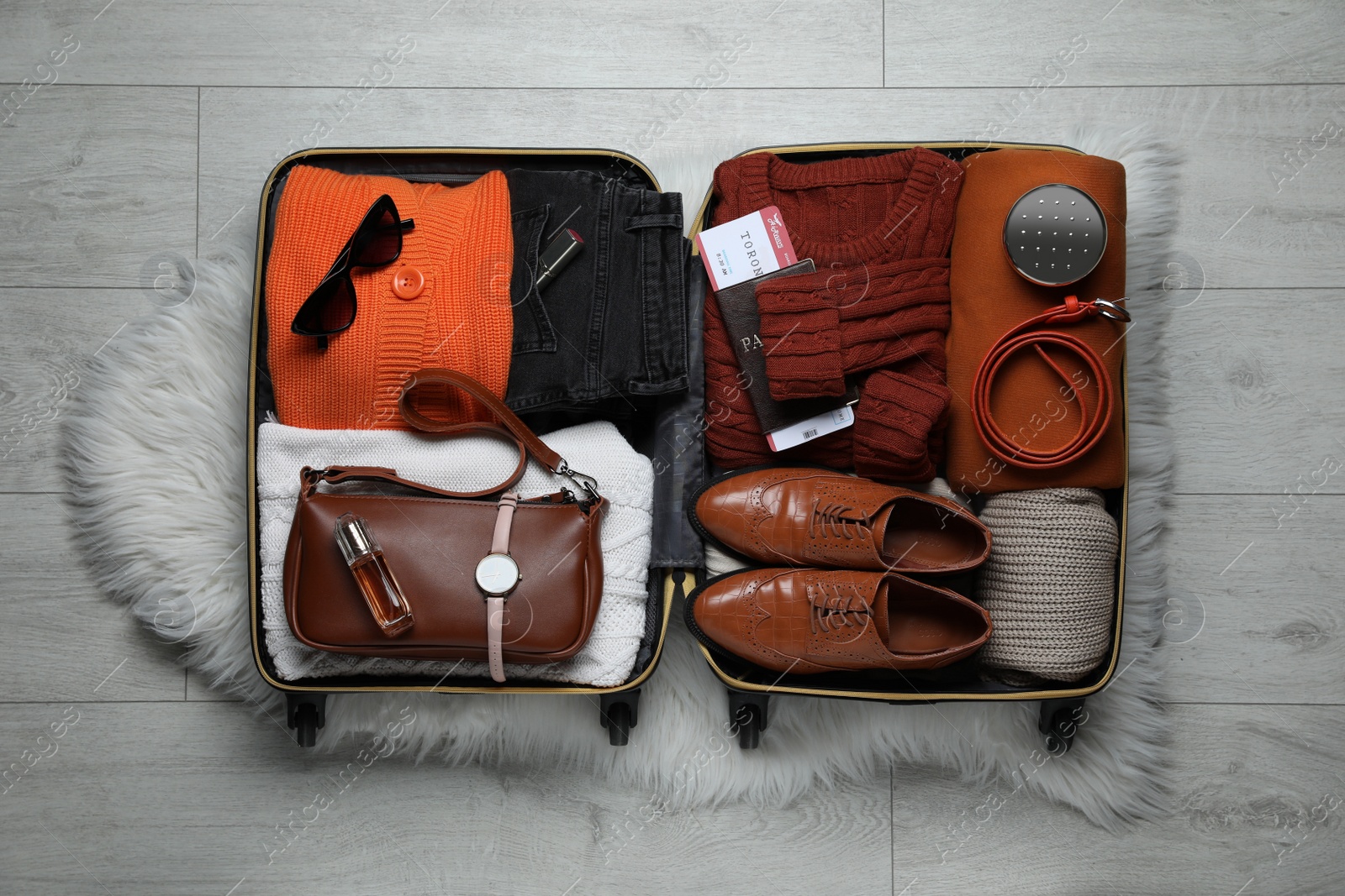 Photo of Open suitcase with folded clothes, accessories and shoes on floor, top view