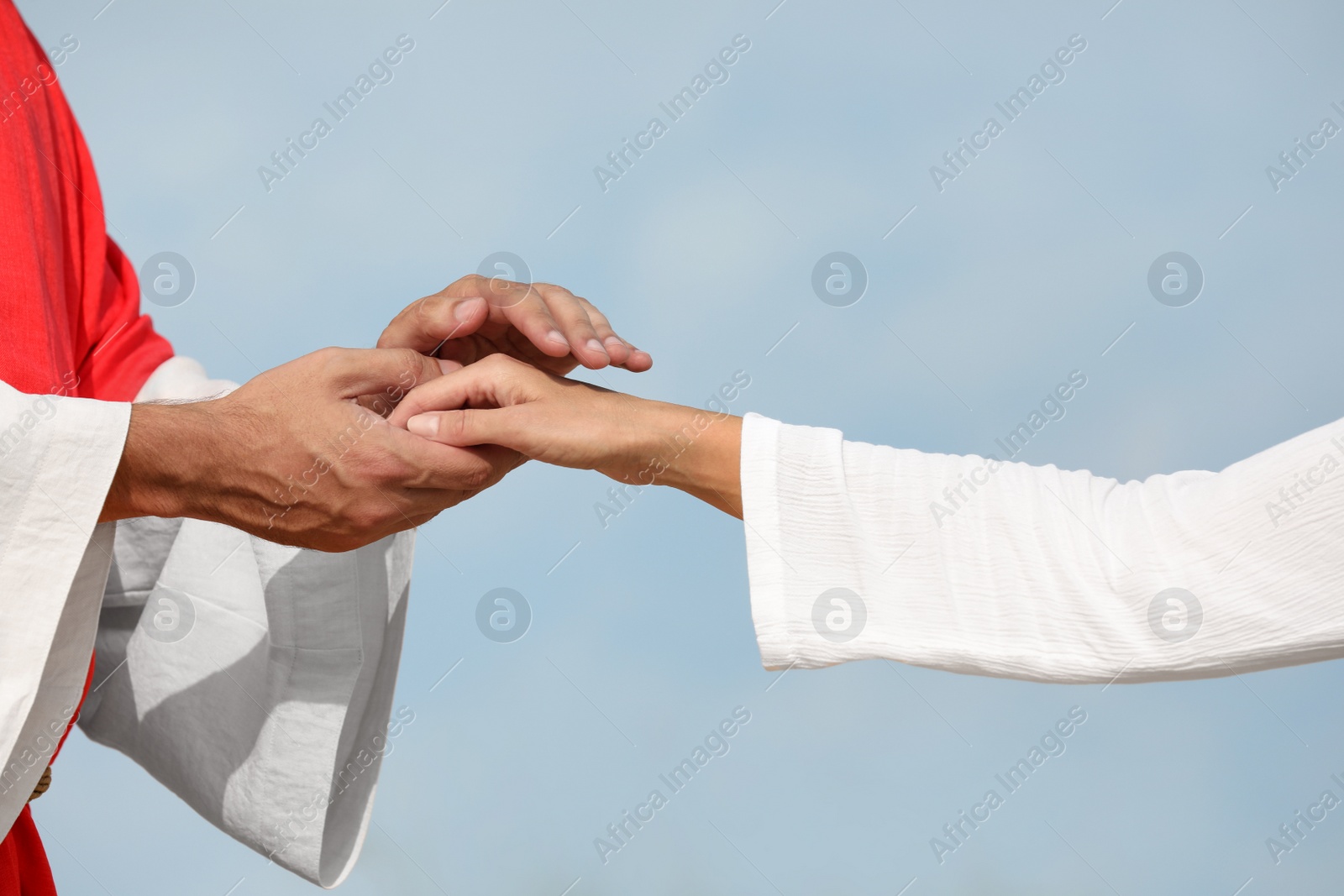 Photo of Jesus Christ holding woman's hand against blue sky, closeup