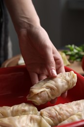 Photo of Woman putting uncooked stuffed cabbage roll into baking dish at table, closeup