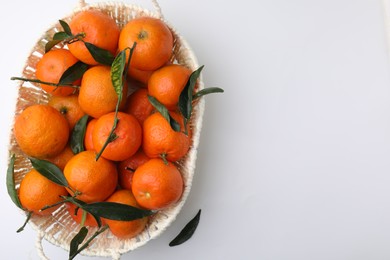 Fresh ripe tangerines and leaves in basket on white table, top view. Space for text