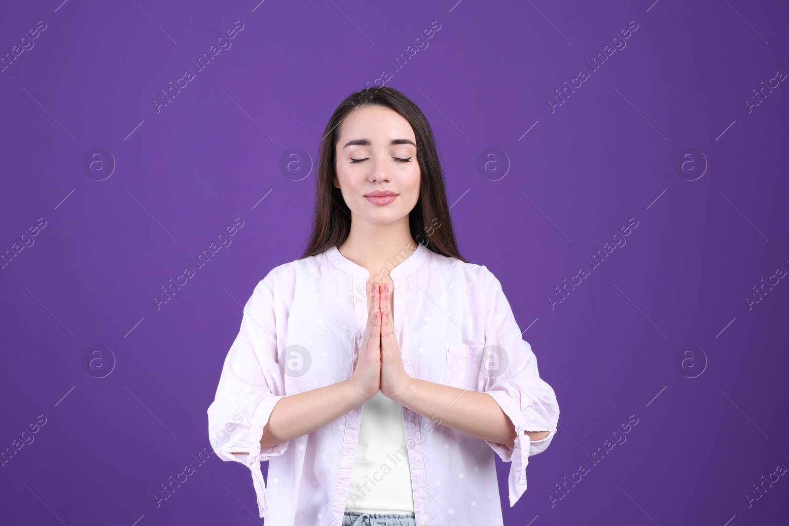 Photo of Young woman meditating on purple background. Stress relief exercise