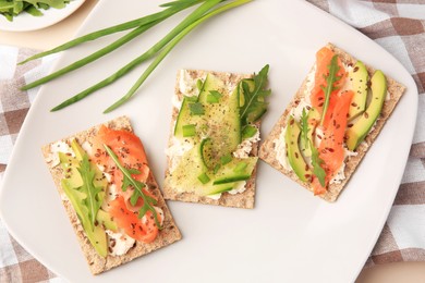 Photo of Fresh crunchy crispbreads with cream cheese, cucumber, green onion, salmon and arugula on plate, flat lay