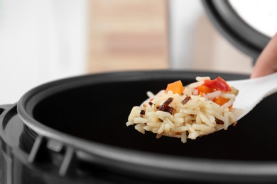Photo of Spoon with prepared rice over multi cooker, closeup