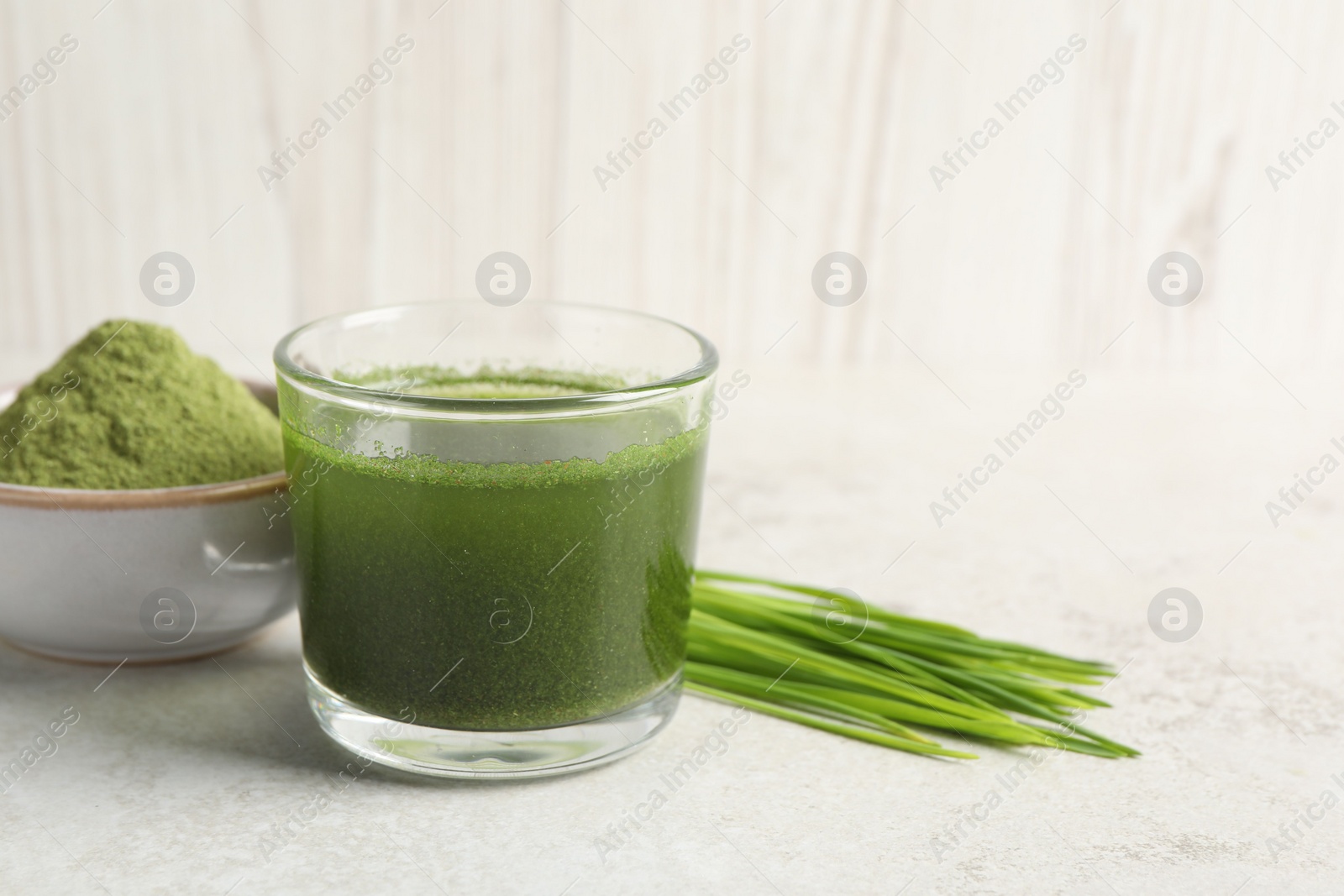 Photo of Wheat grass drink in glass, fresh sprouts and bowl of green powder on light table. Space for text