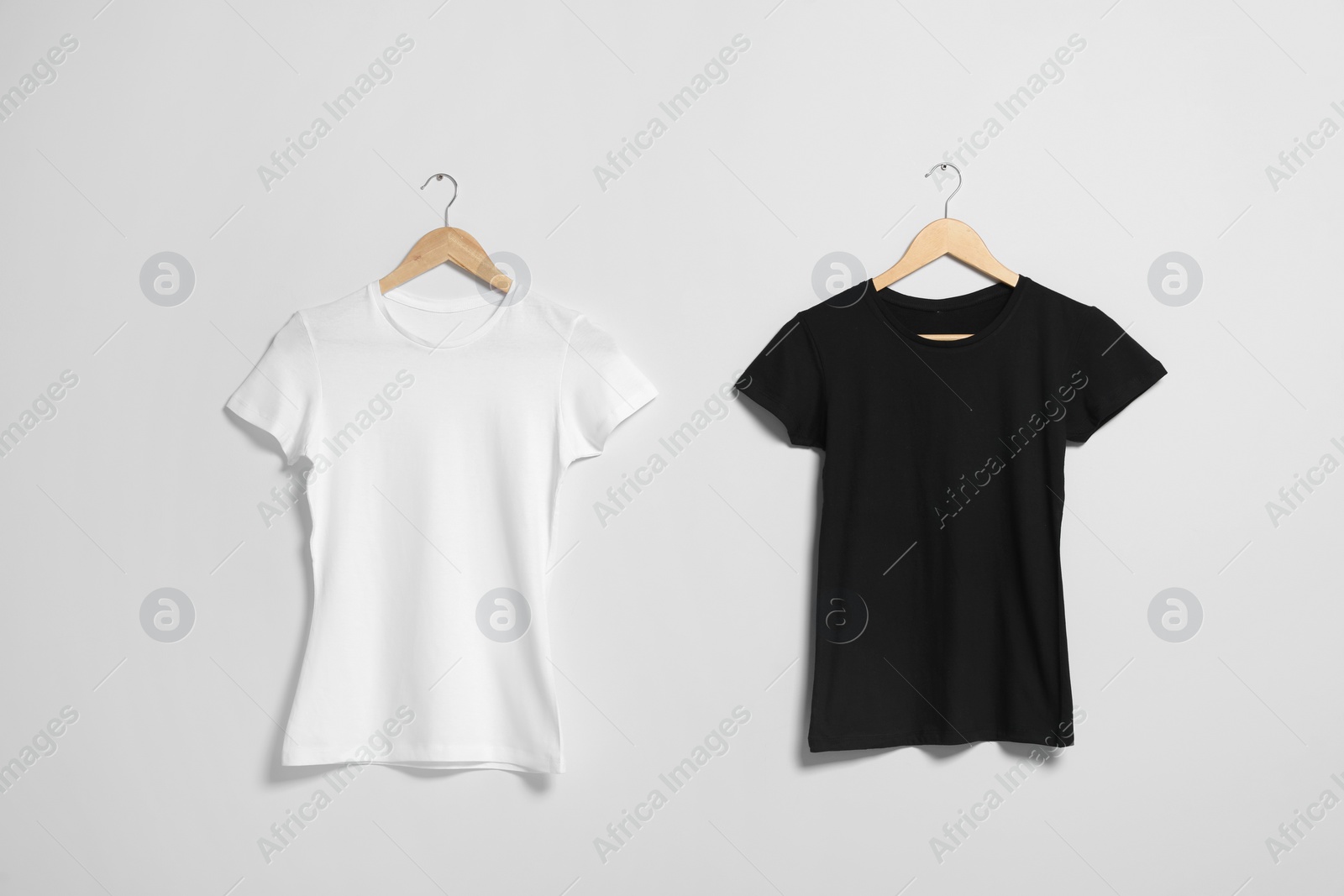 Photo of Hangers with different t-shirts on light wall. Mockup for design