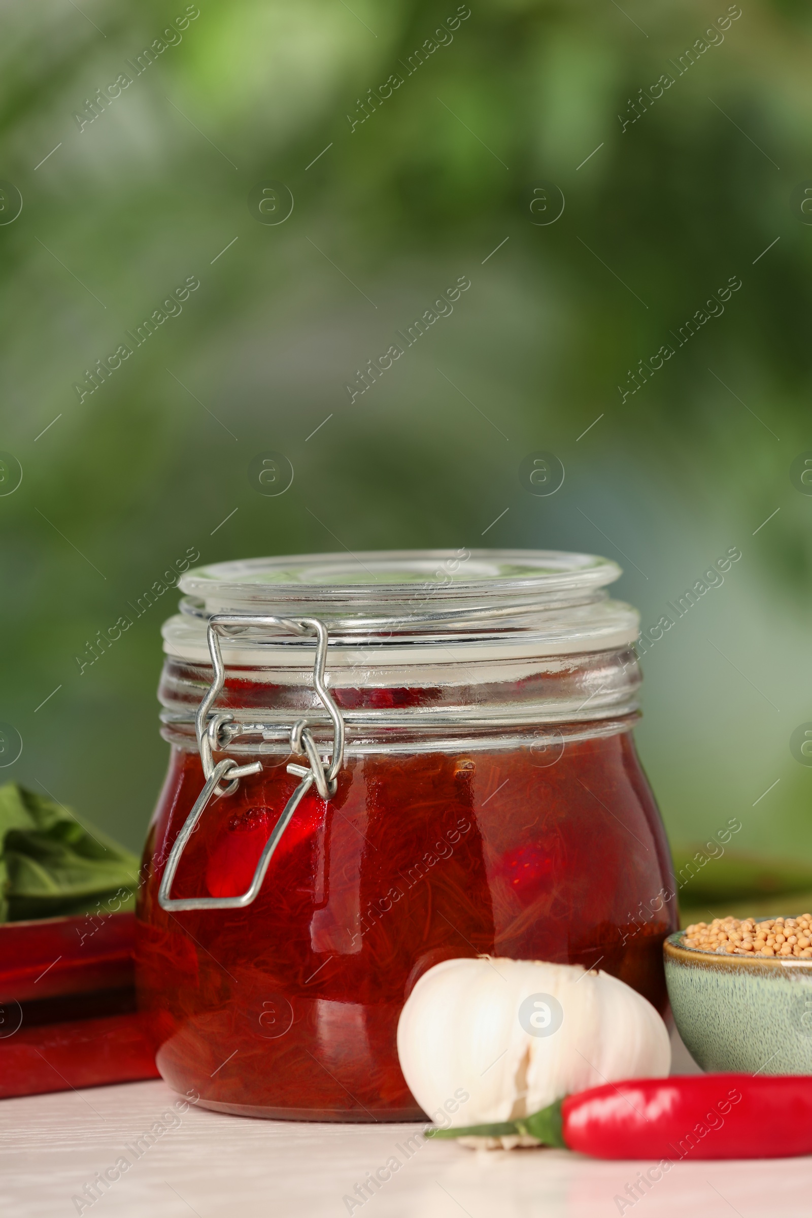 Photo of Tasty rhubarb sauce and ingredients on white table against blurred background, space for text
