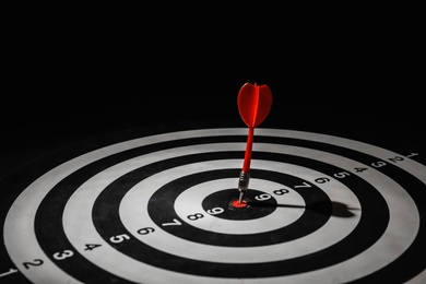 Photo of Red arrow hitting target on dart board against black background