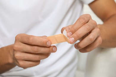 Photo of Young man opening sticking plaster, closeup view