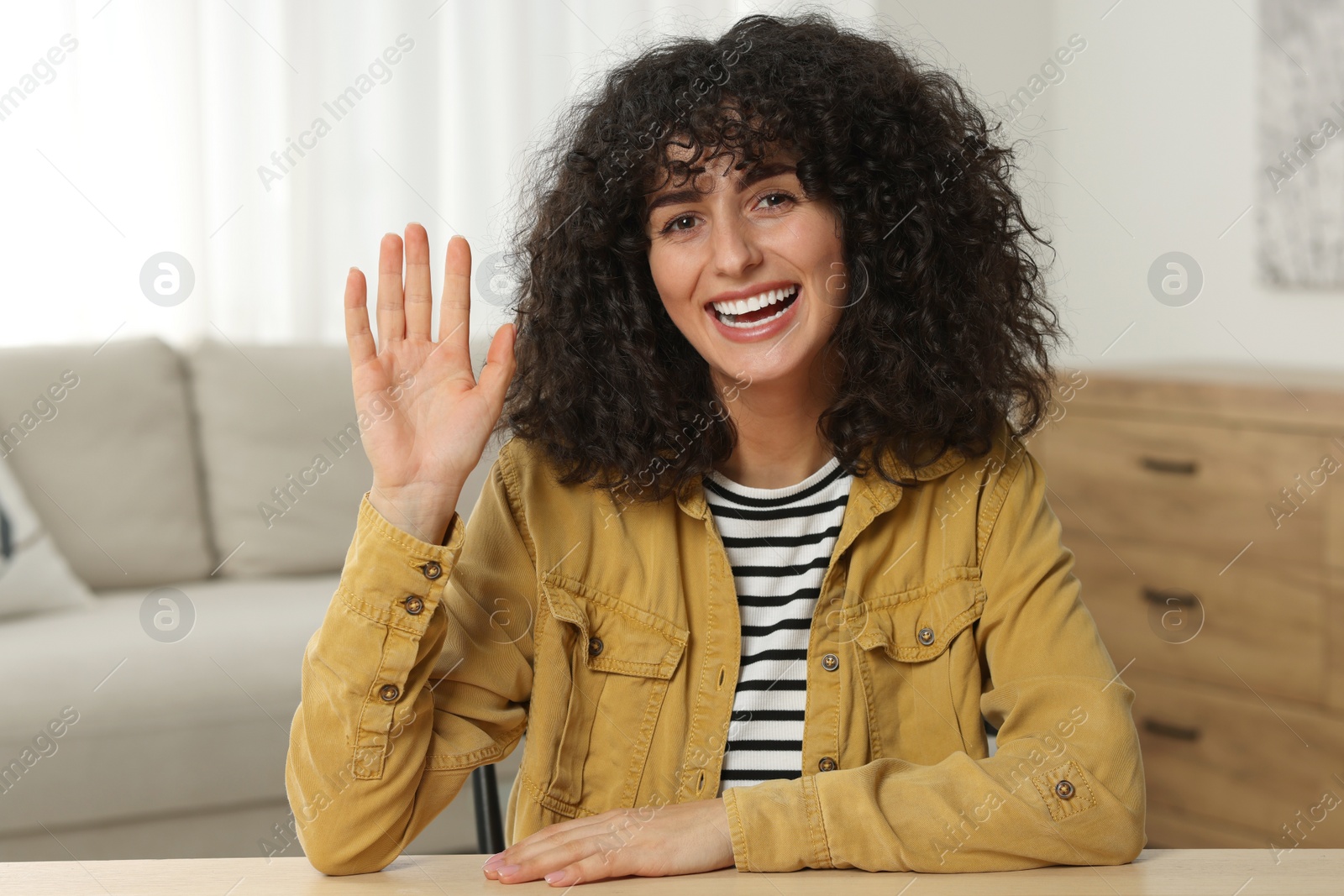 Photo of Happy woman waving hello at wooden table in room