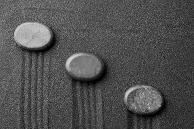 Photo of Zen garden stones on black sand with pattern, top view