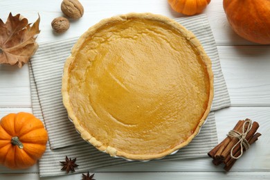Delicious pumpkin pie and ingredients on white wooden table, flat lay