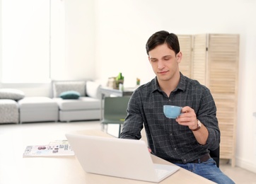 Portrait of confident young man with  laptop and cup at table