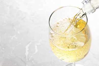 Pouring tasty aromatic wine in glass at gray marble table, closeup. Space for text