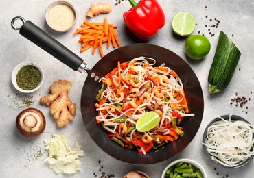 Shrimp stir fry with noodles and vegetables in wok surrounded by ingredients on grey table, flat lay