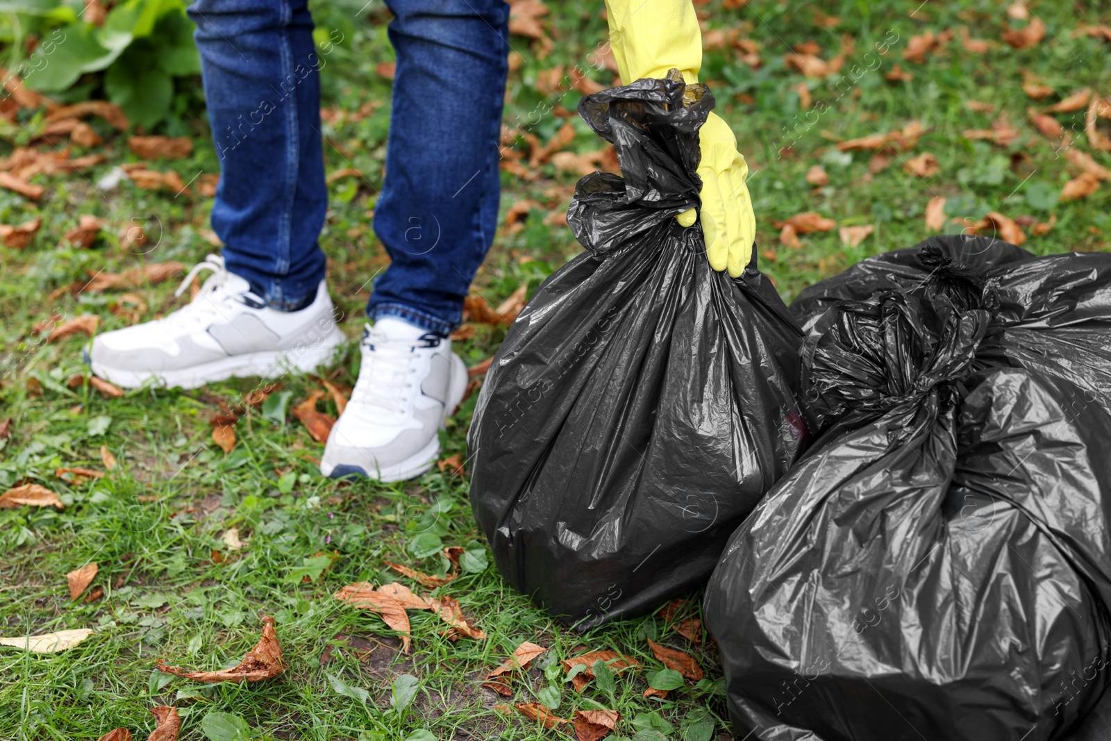 Photo of Man holding plastic bags with garbage in park, closeup.