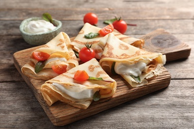 Thin pancakes with sour cream and cherry tomatoes on wooden board