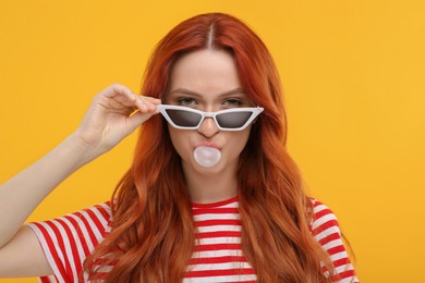 Photo of Beautiful woman in sunglasses blowing bubble gum on orange background