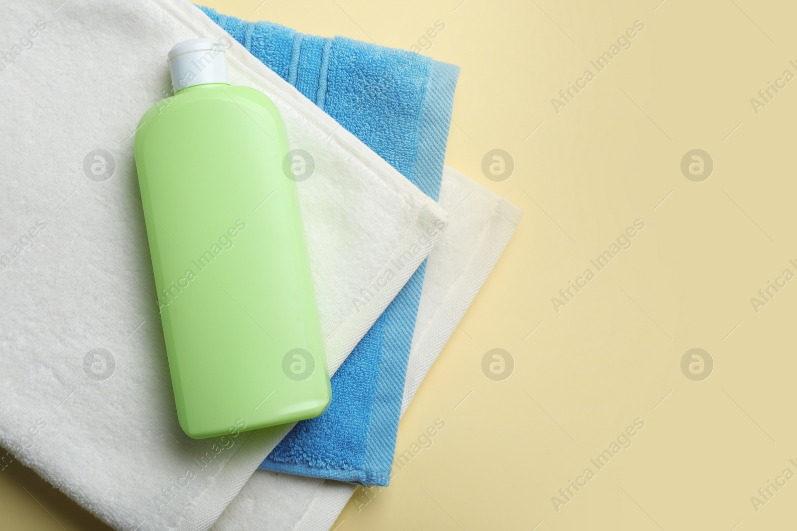 Photo of Bottle of shampoo and towels on color background, top view with space for text