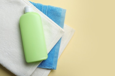 Bottle of shampoo and towels on color background, top view with space for text