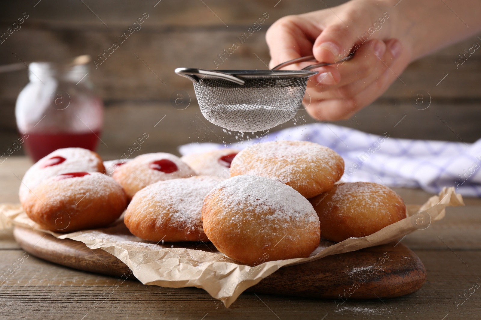 Photo of Woman dusting powdered sugar onto delicious Hanukkah donuts on wooden table, closeup