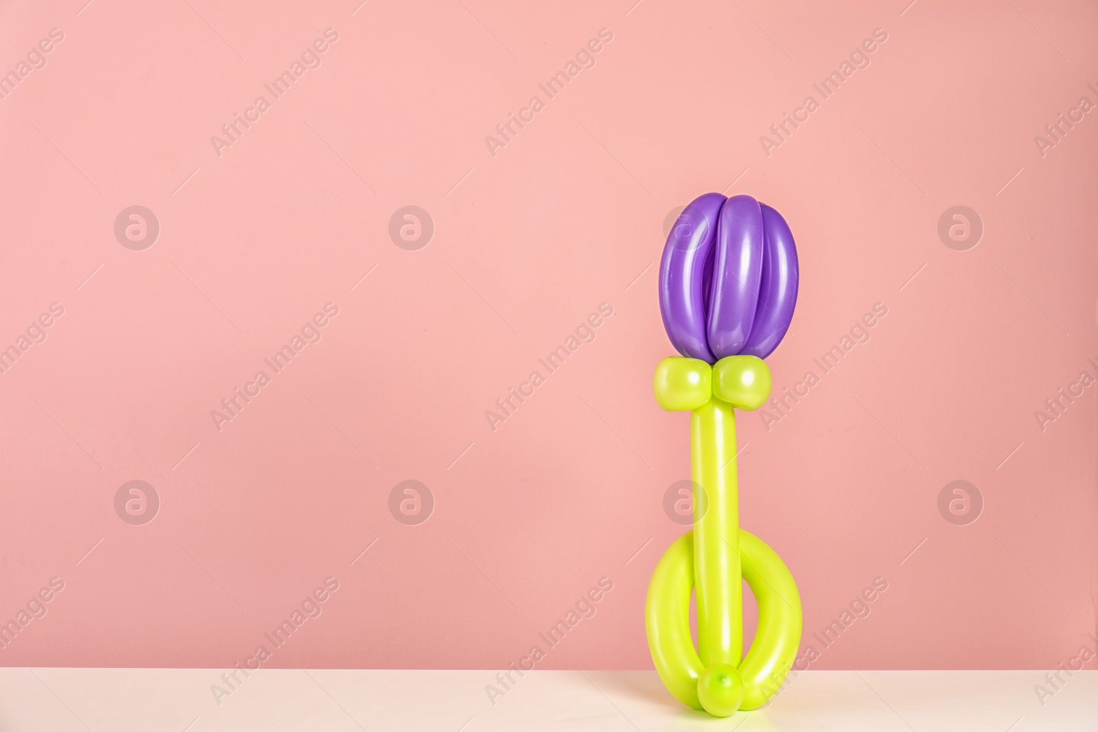 Photo of Flower figure made of modelling balloon on table against color background. Space for text