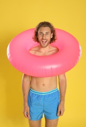 Photo of Attractive young man in swimwear with pink inflatable ring on yellow background