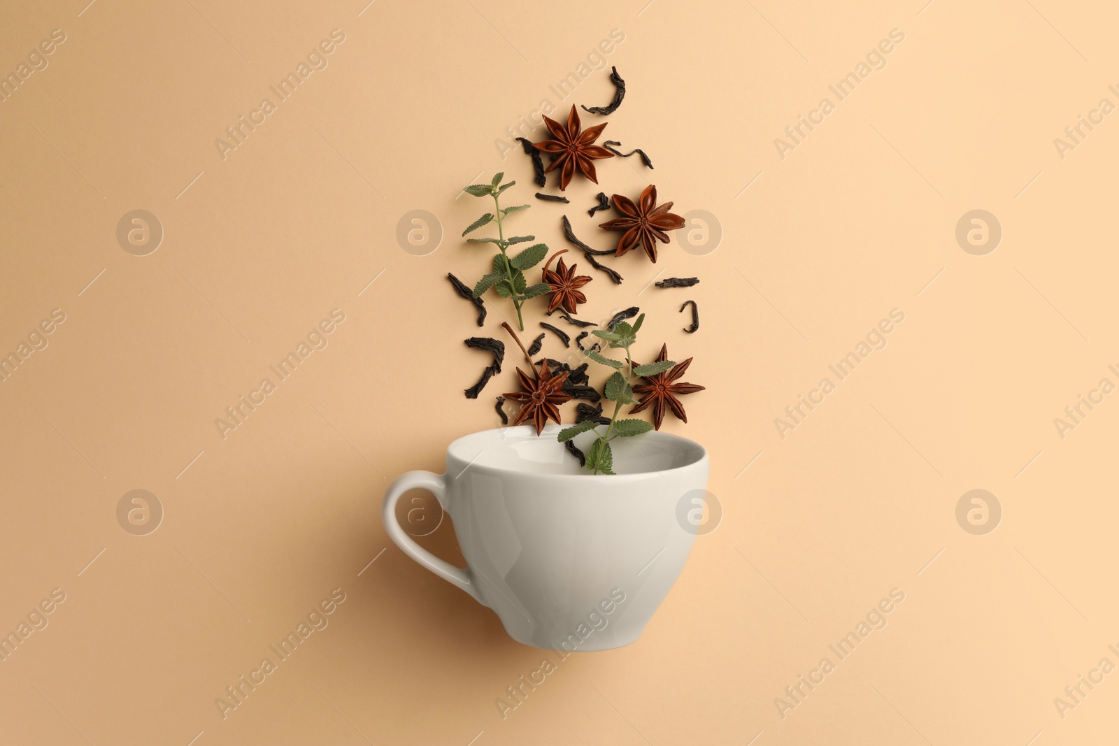 Photo of Anise stars, dry tea and mint falling into cup on beige background, flat lay