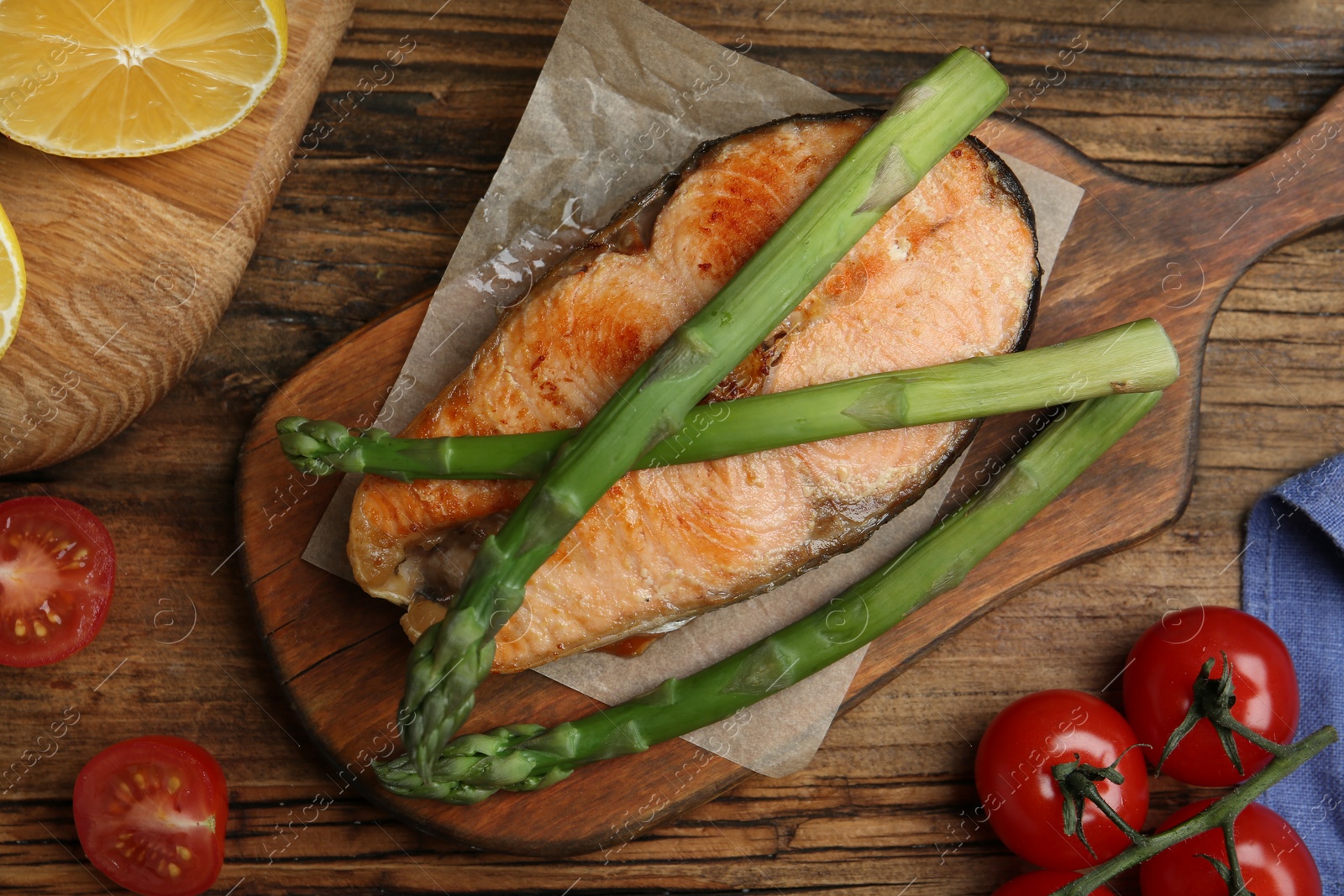 Photo of Tasty salmon steak served with asparagus on wooden table, flat lay