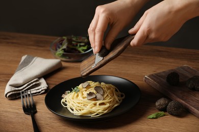 Photo of Woman slicing truffle onto spaghetti at wooden table, closeup