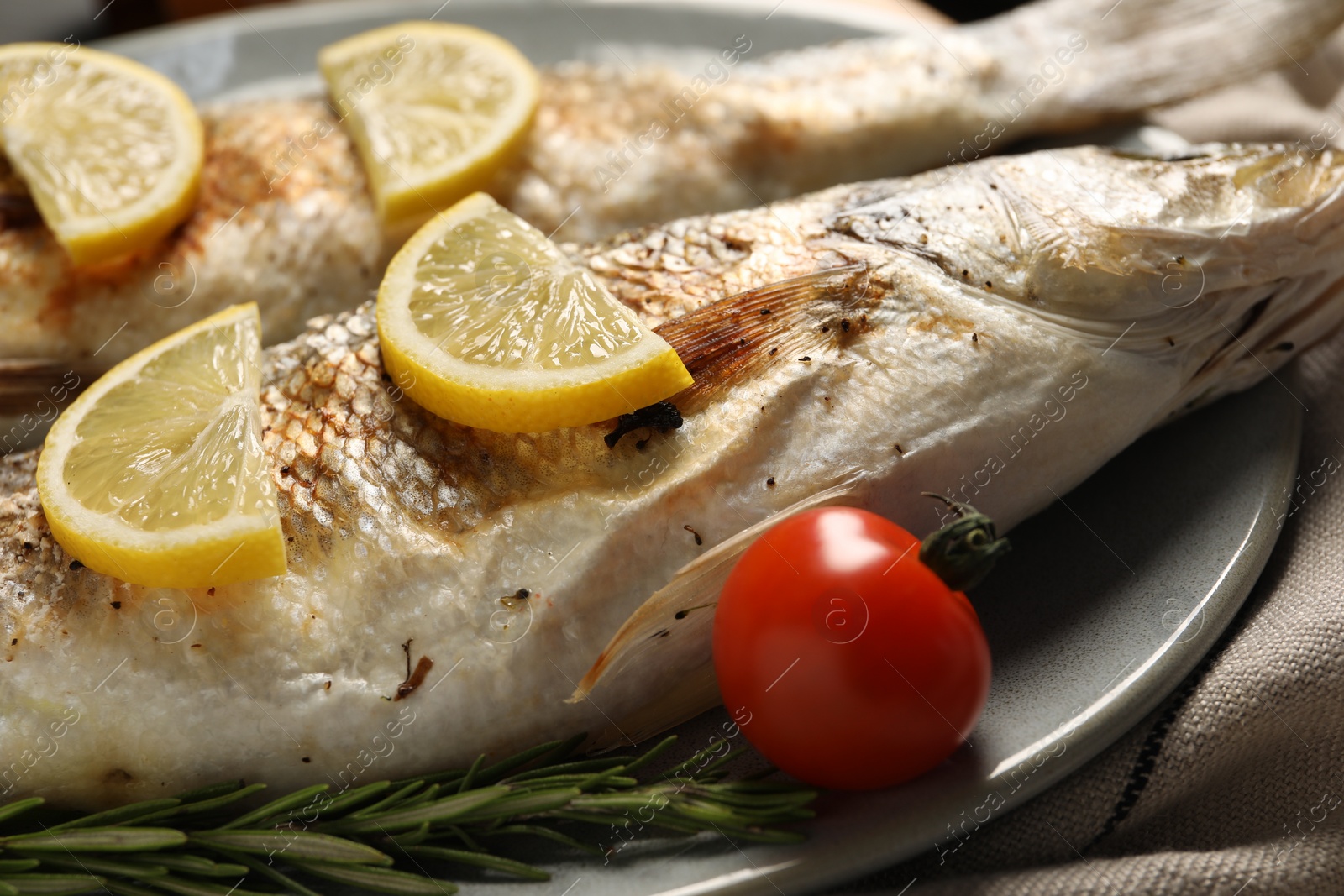 Photo of Delicious baked fish, tomato, lemon and rosemary on plate, closeup