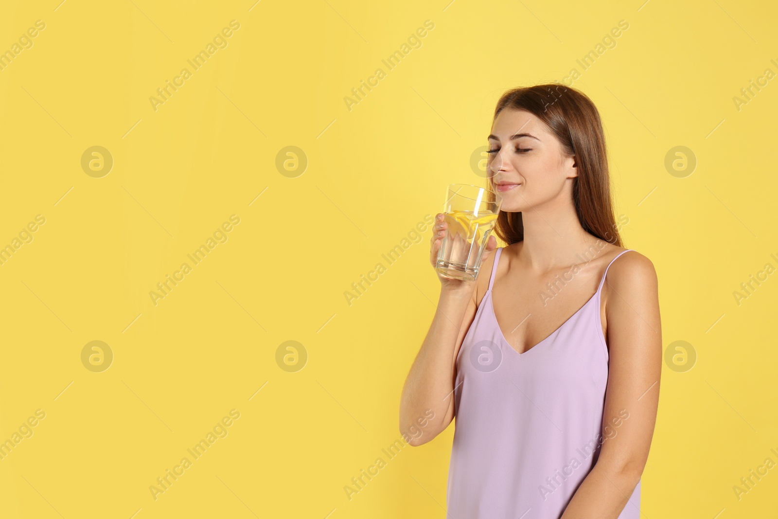 Photo of Young woman drinking lemon water on yellow background. Space for text