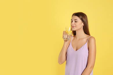 Young woman drinking lemon water on yellow background. Space for text