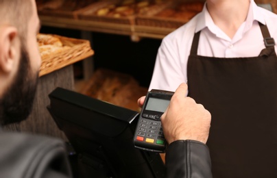 Photo of Man with credit card using payment terminal at shop, closeup