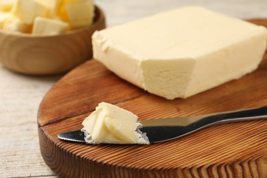 Photo of Tasty butter and knife on light wooden table, closeup