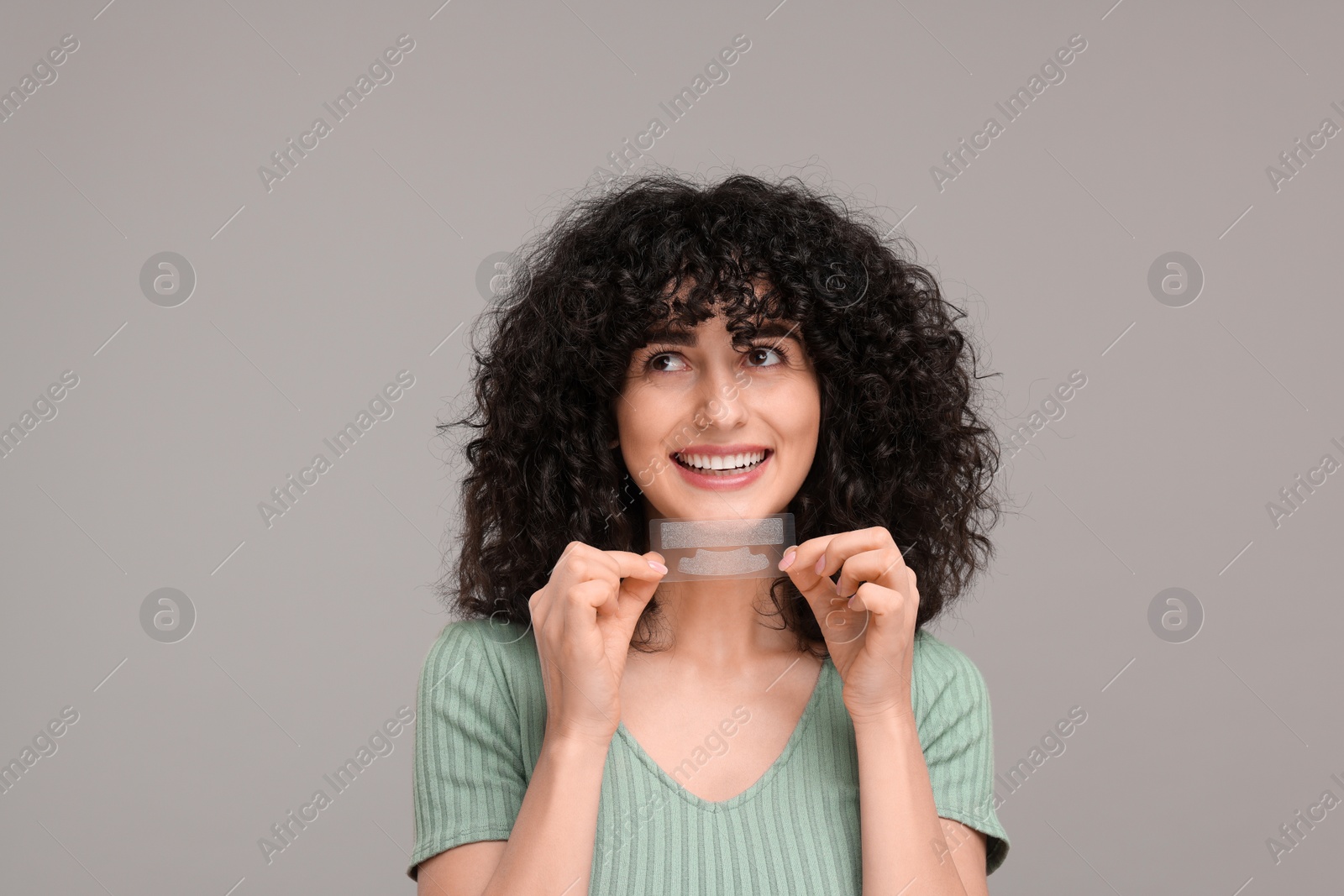 Photo of Young woman holding teeth whitening strips on grey background