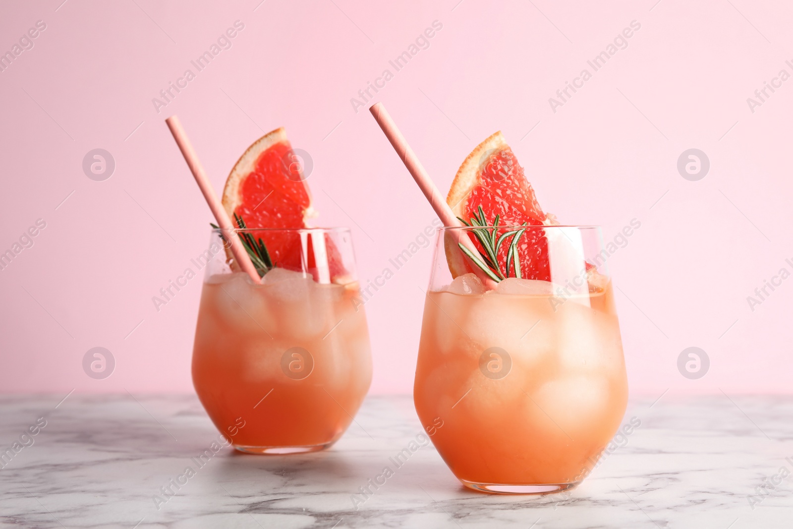 Photo of Glasses of grapefruit cocktail on table against color background