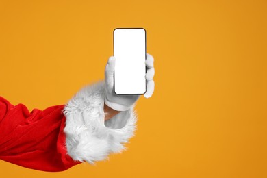 Photo of Merry Christmas. Santa Claus showing smartphone on orange background, closeup. Mockup for design