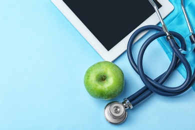 Stethoscope, tablet and apple on color background. Medical equipment