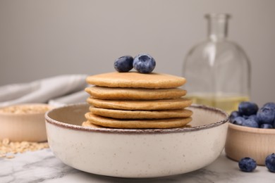 Tasty oatmeal pancakes with blueberries on white marble table, closeup