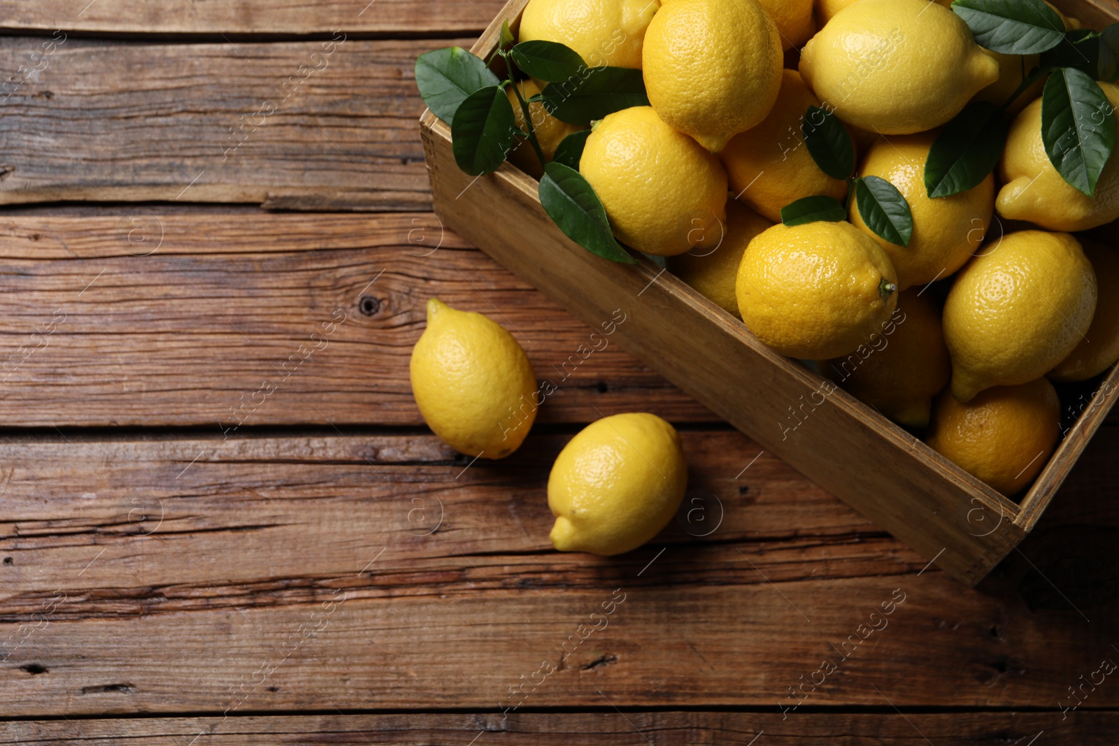 Photo of Fresh lemons in crate on wooden table, top view. Space for text