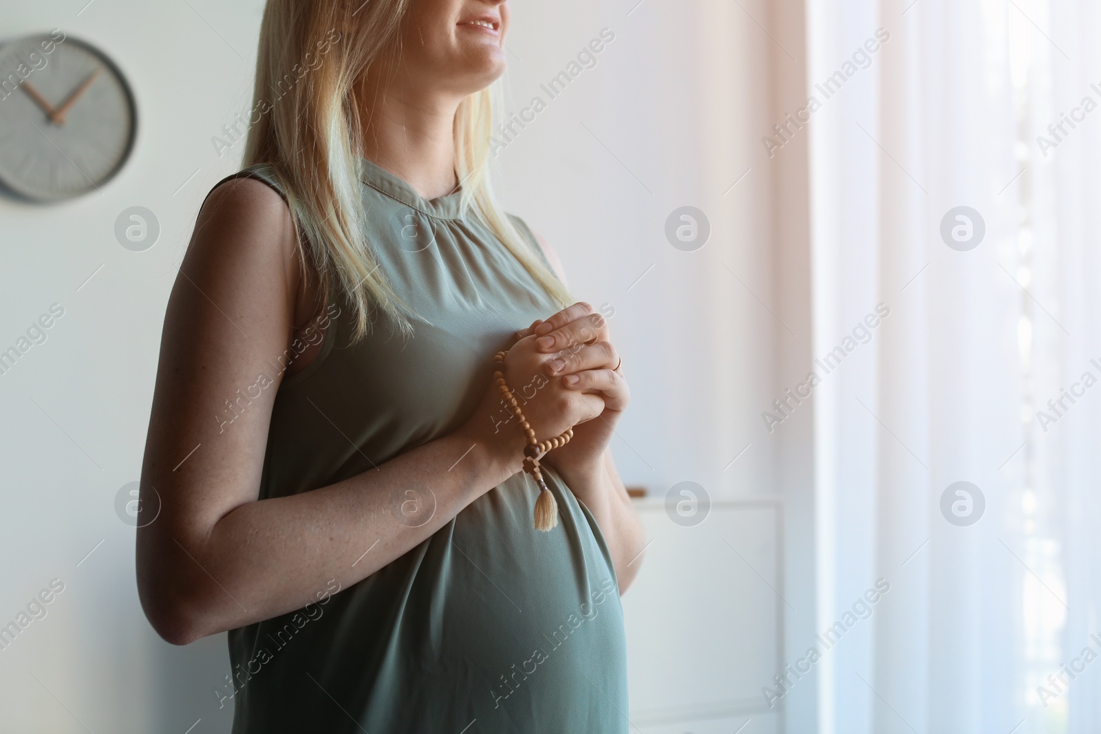 Photo of Young pregnant woman with beads praying at home. Space for text