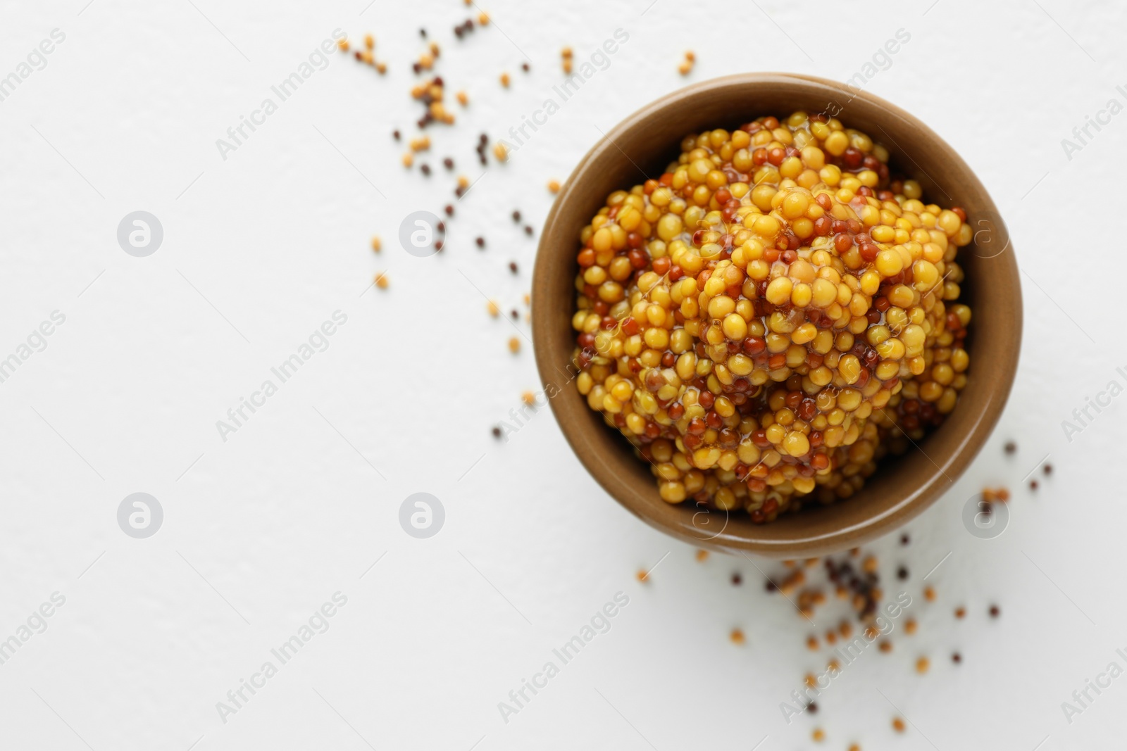 Photo of Fresh whole grain mustard in bowl and dry seeds on white table, flat lay. Space for text