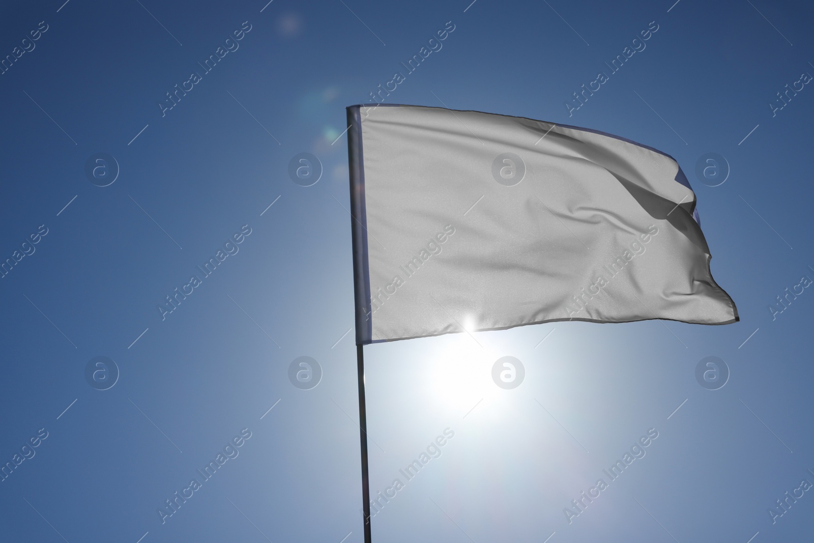 Photo of White flag fluttering against blue sky on sunny day