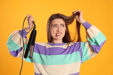 Photo of Stressed young woman with flattening iron on yellow background. Hair damage