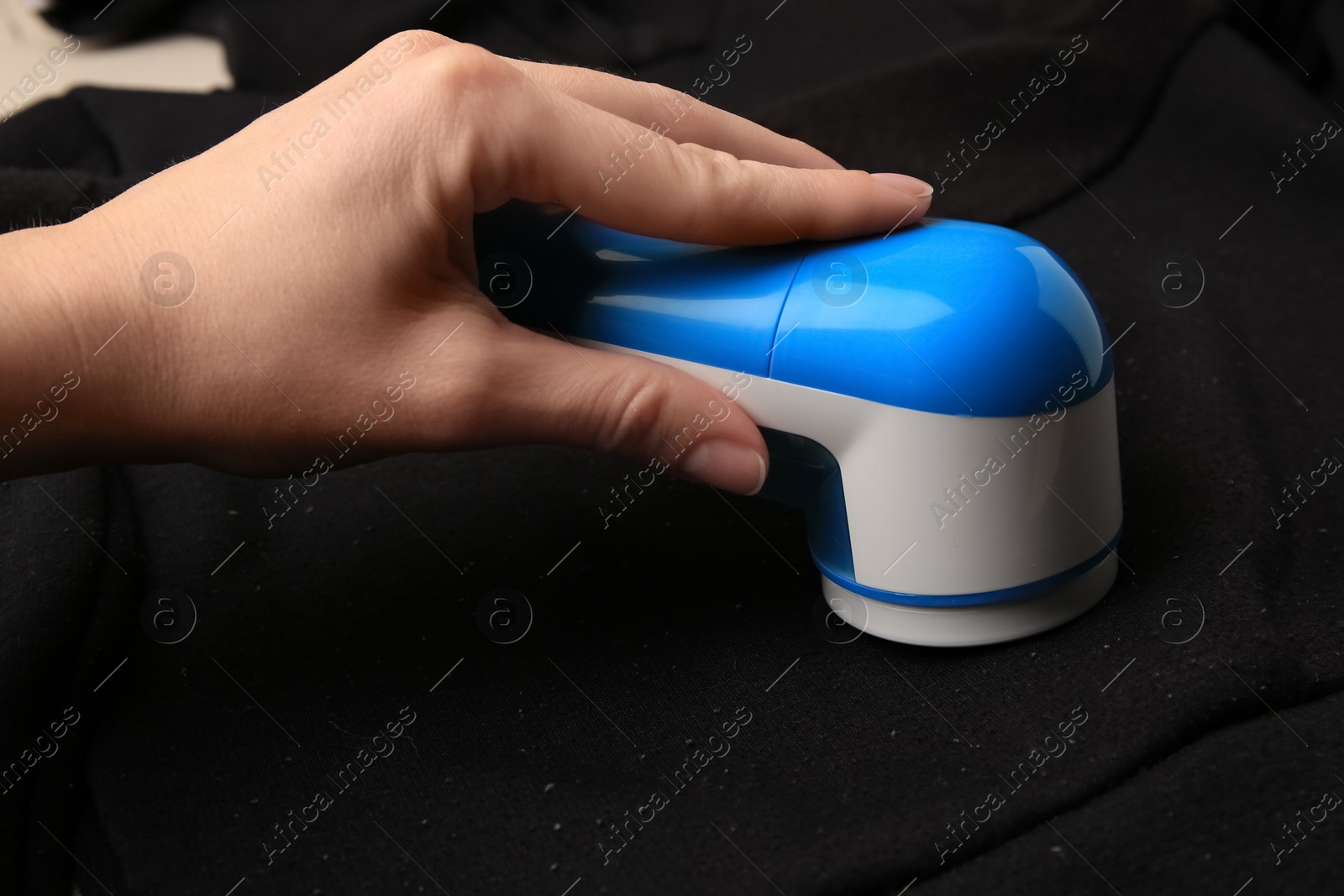 Photo of Woman using fabric shaver on black cloth with lint, closeup