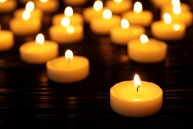 Photo of Many burning candles on table in darkness, space for text