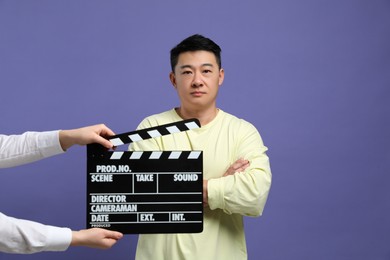 Photo of Asian actor performing while second assistant camera holding clapperboard on purple background. Film industry