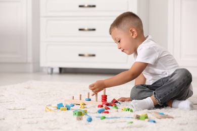 Photo of Motor skills development. Little boy playing with stacking and counting game on floor indoors