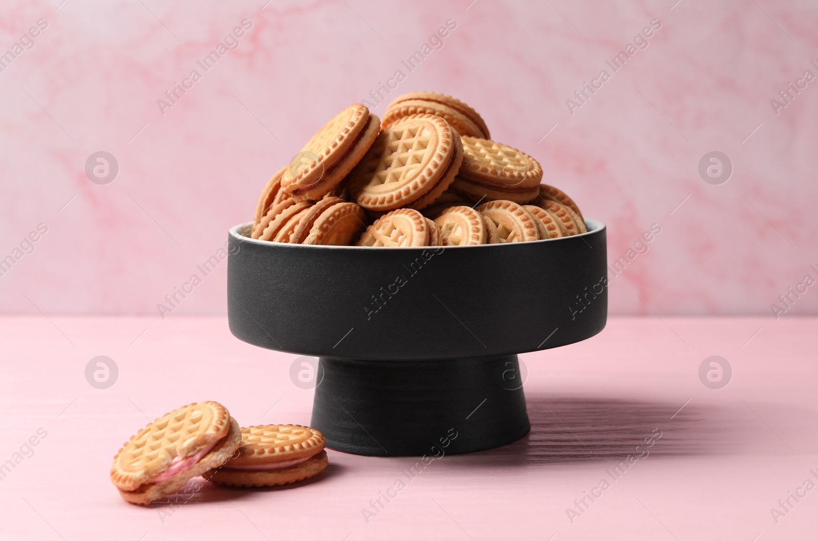 Photo of Tasty sandwich cookies with cream on pink wooden table